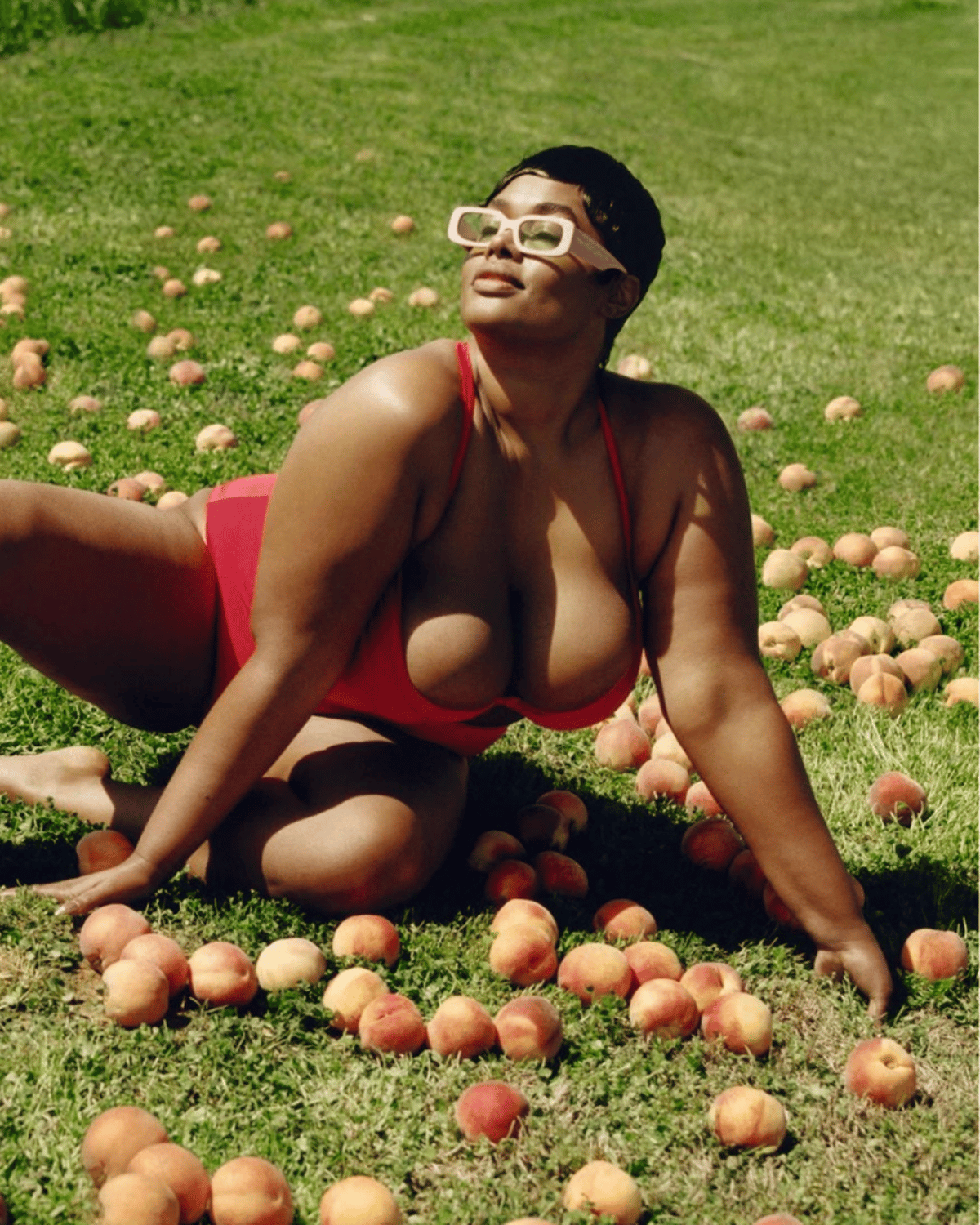Precious Lee in a red bikini laying on the ground surrounded by apples