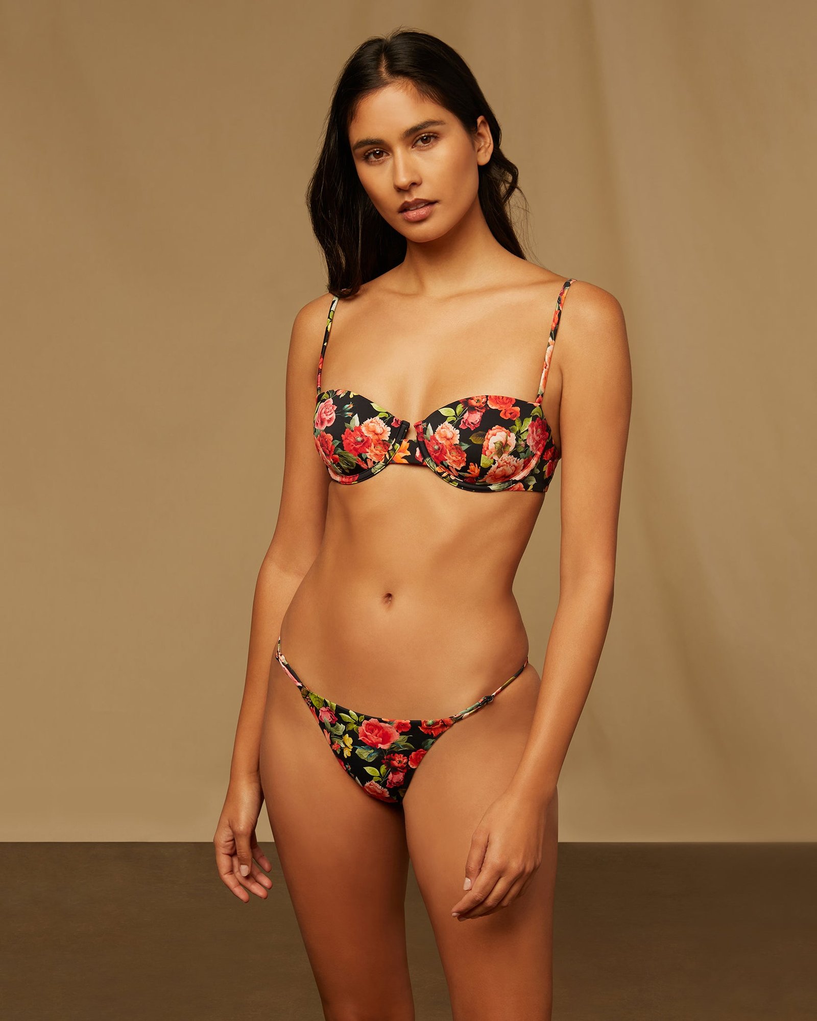 Model in the Dalia Top and Hannah Bottom in Black Multi, a black bikini with red and pink roses, against a beige backdrop