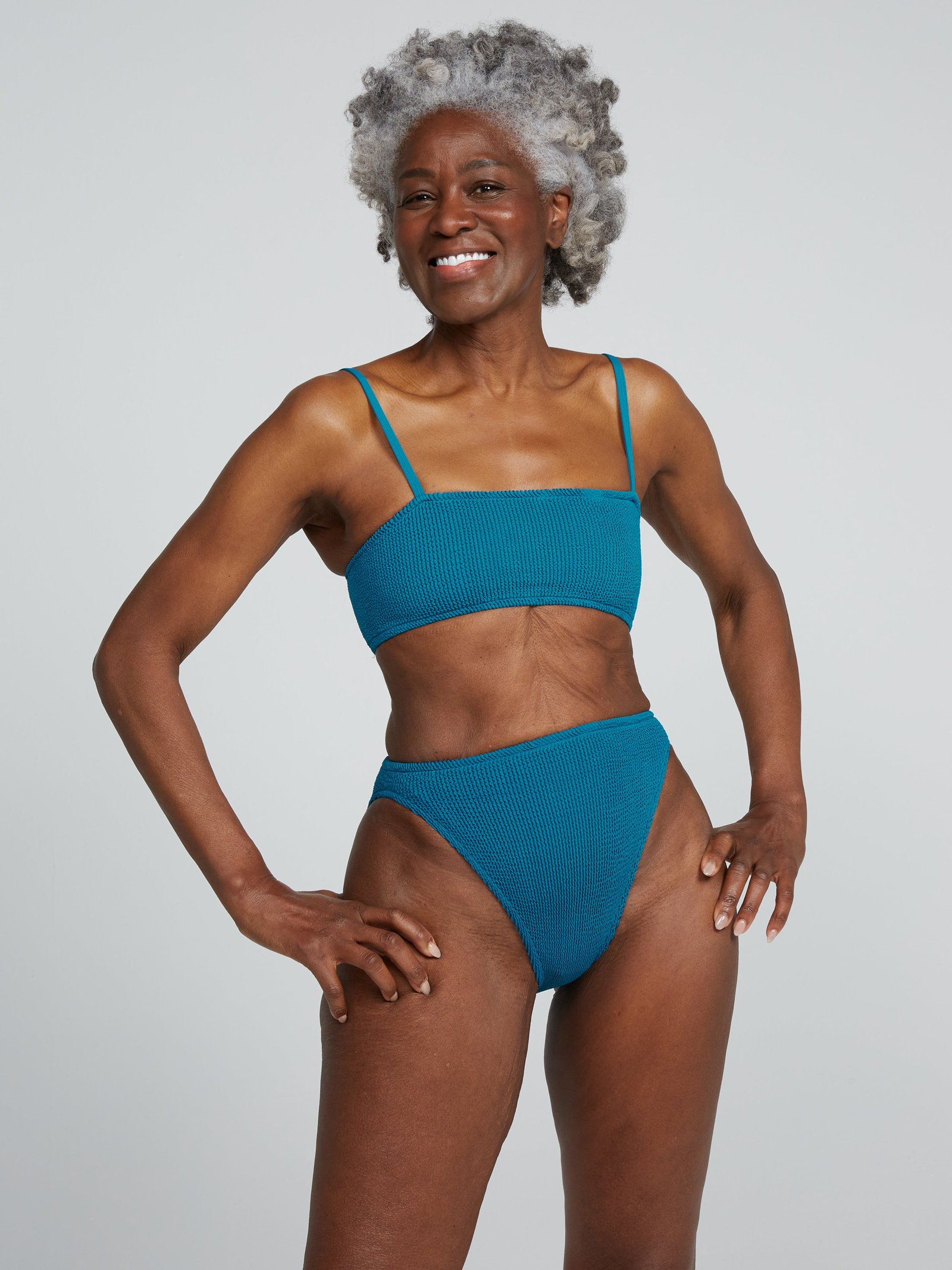 Smiling grey-haired woman in Youswim's Poise Standard Waist Two-Piece, a teal crinkle bandeau top with high-cut bottom