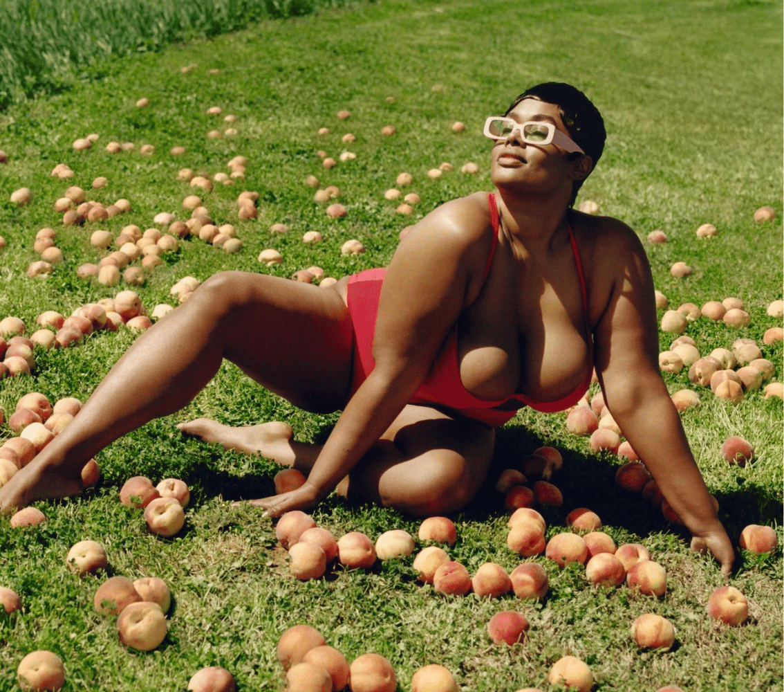 Precious Lee  in a red bikini laying on the ground surrounded by apples