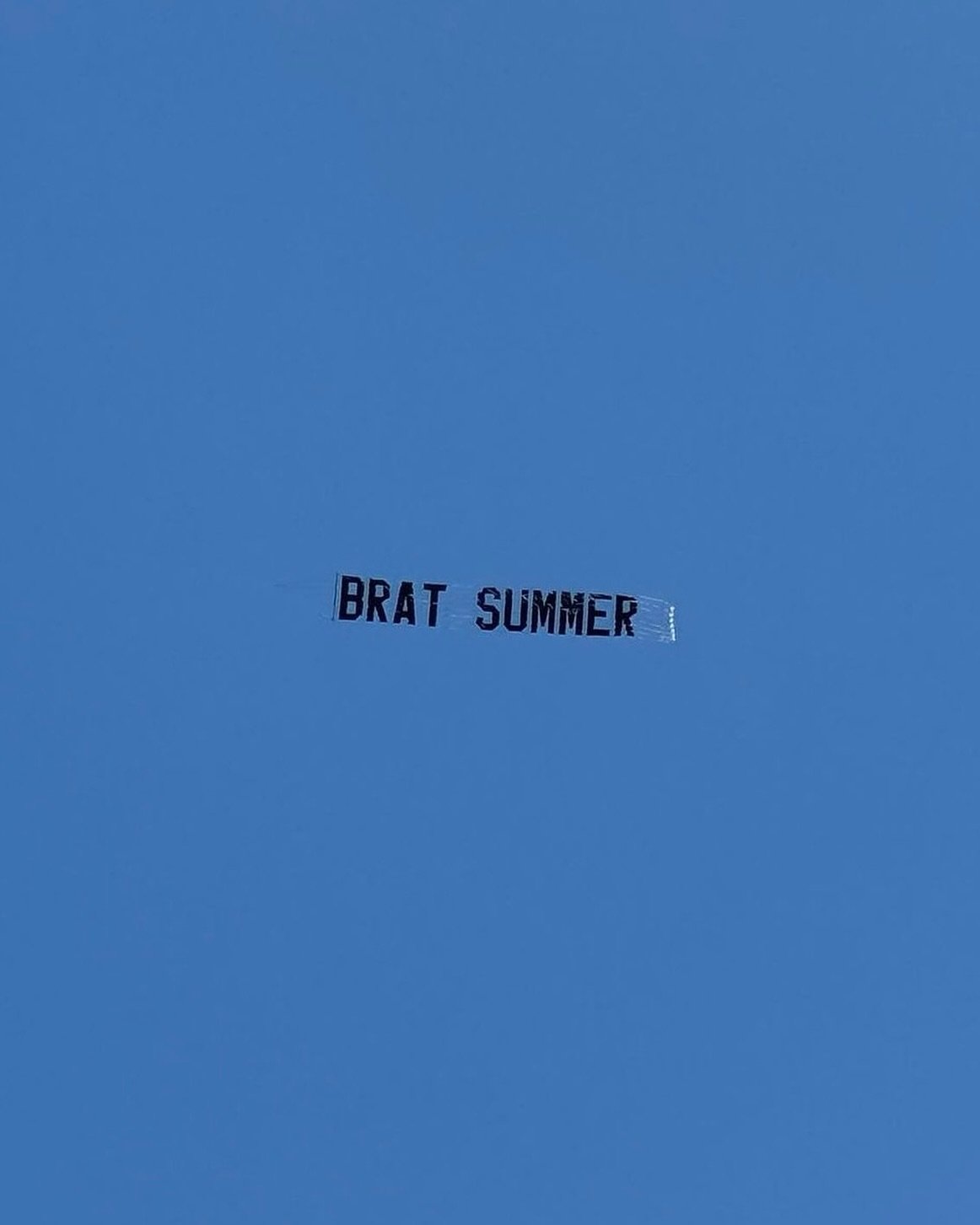 A plane banner reading "BRAT SUMMER" against a blue sky