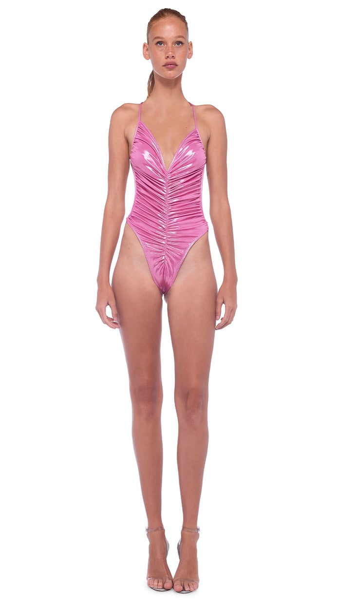 Model in Norma Kamali's Marissa one-piece in bubble gum pink metallic, ruched down the front with a deep V-neck