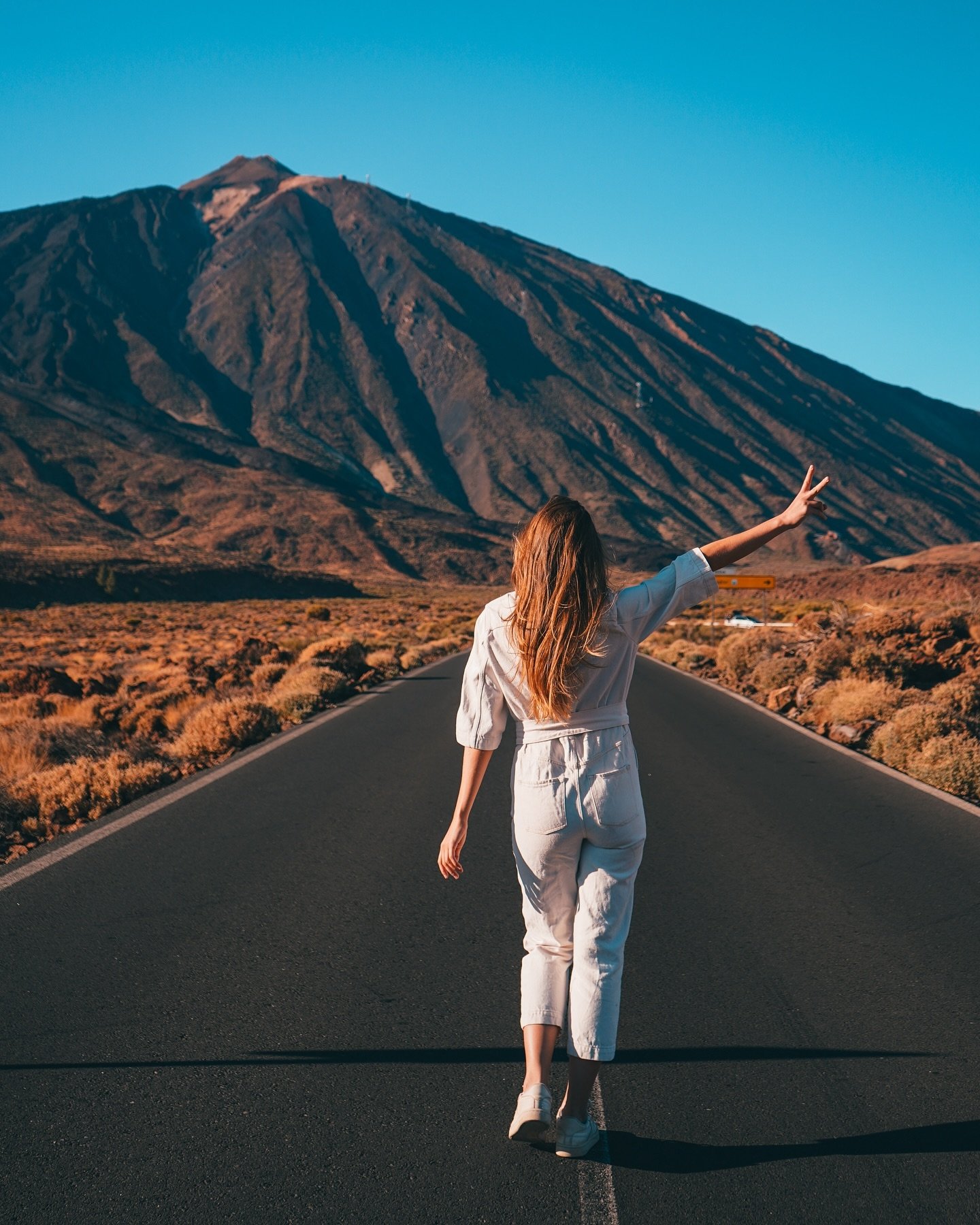 Sigrid Rijckoort seen from behind in a white jumpsuit, walking down a road towards a volcano