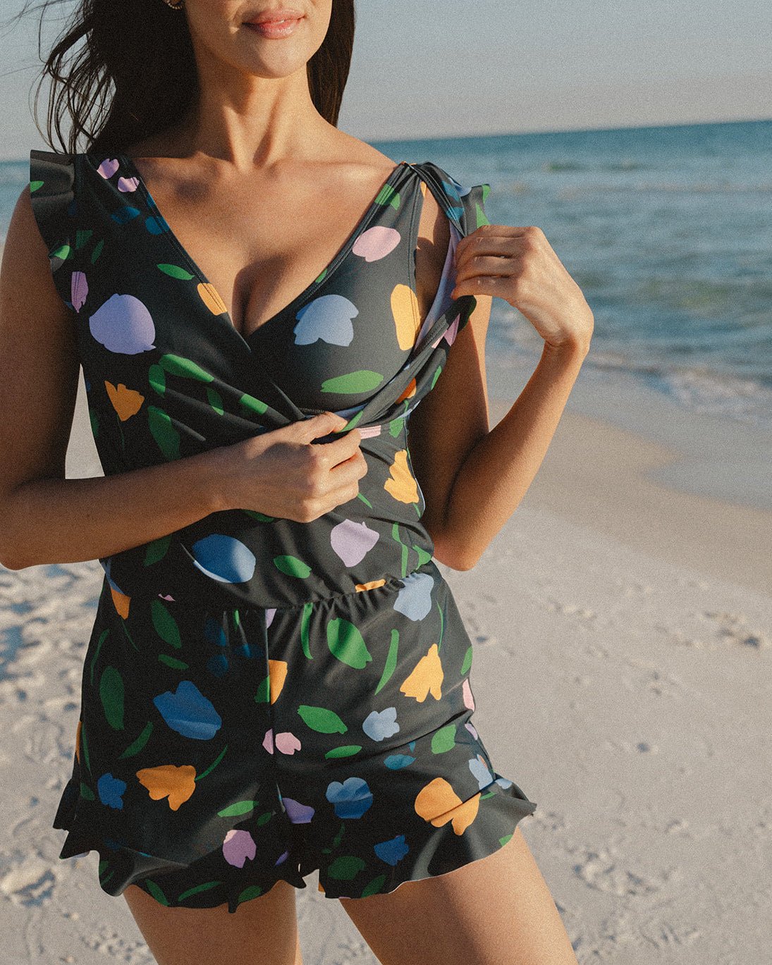 Woman on the beach in the Ginger Swim Romper, a black wrap-front romper printed with pastel petals