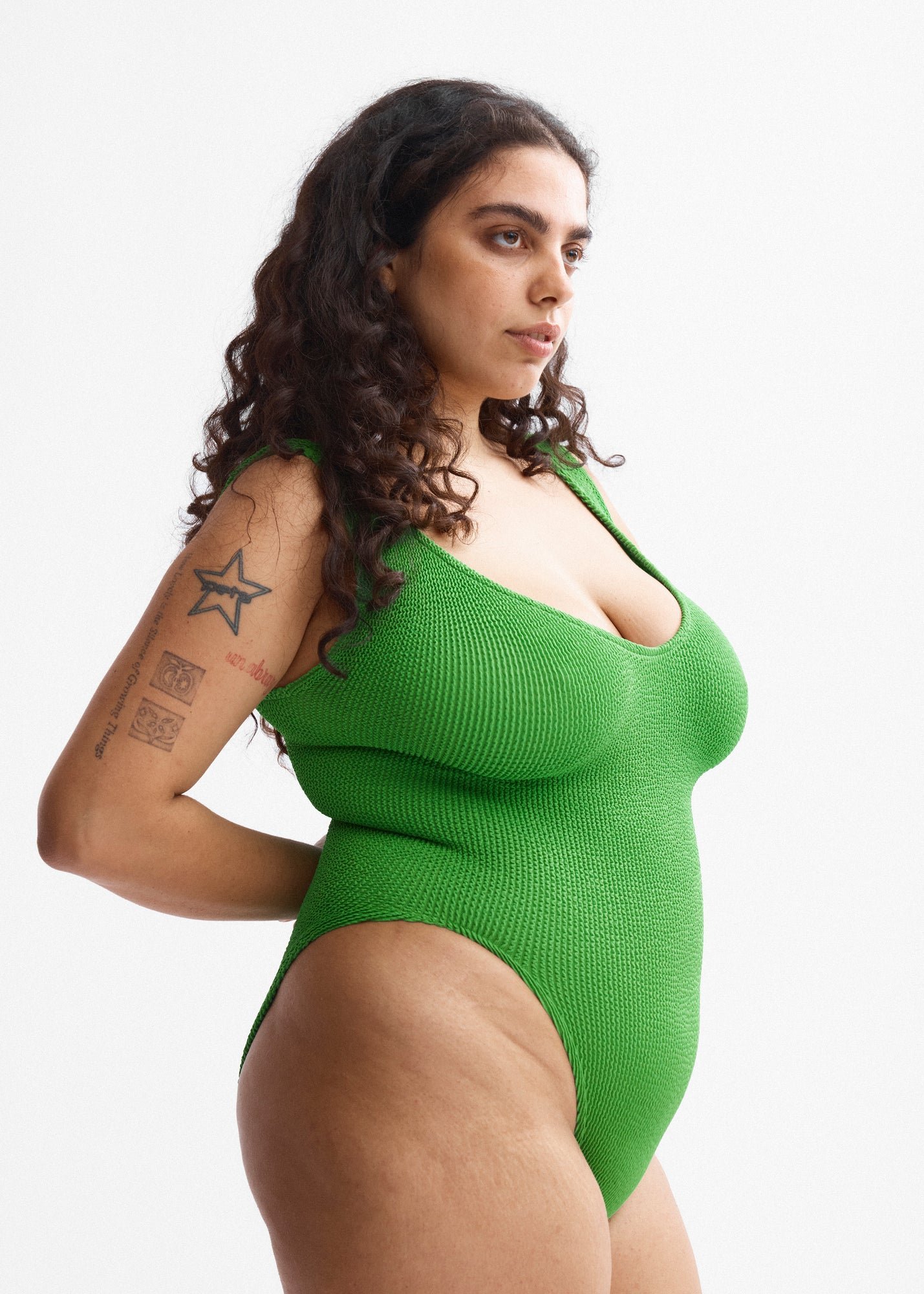 Side view of the Eva One-Piece in bright green crinkle fabric, on a model with a star tattoo