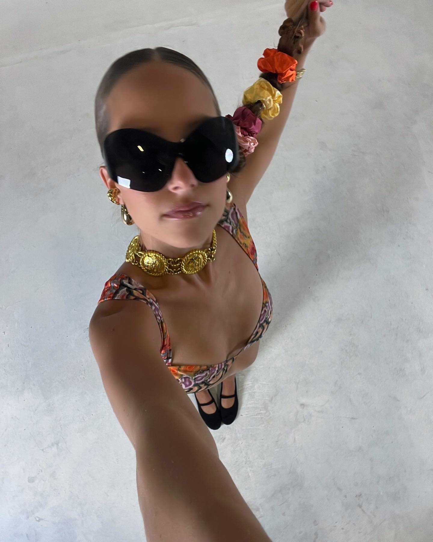 Georgia in a floral bikini, oversized black sunglasses and a gold chain choker, flowers in her ponytail