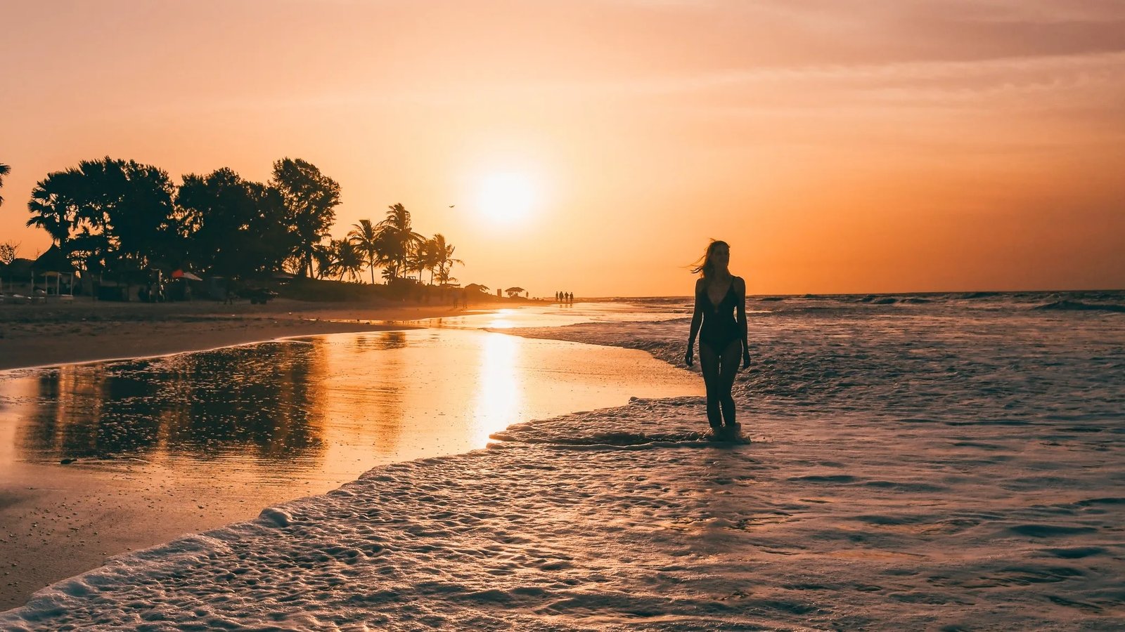 Sigrid Rijckoort in a swimsuit, silhouetted against the sunset as she walks through the shallow waves