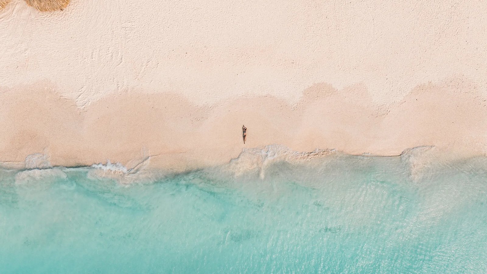 Aerial view of a sandy beach with turquoise waves and Sigrid Rijckoort lying near the shoreline